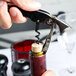 A hand using a Franmara two-lever corkscrew with a black handle to open a wine bottle.