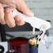 A person using a Franmara Boomerang Waiter's Corkscrew with a white handle to open a wine bottle.