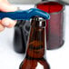 A hand using a dark blue Franmara Traveler's plastic bottle opener to open a brown bottle.