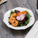 A plate of Villeroy & Boch white bone porcelain salad with shrimp, radishes, and carrots with a fork.