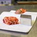 A stainless steel diamond-shaped food mold on a plate of food.