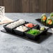 A rectangular black melamine ramekin platter with sushi on it.