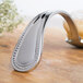 A Bon Chef stainless steel sombrero tasting spoon with a silver handle on a wood surface.