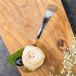 A Bon Chef Reflections bouillon tasting spoon filled with blueberries on a wooden surface.