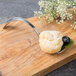 A Bon Chef Tuscany bouillon spoon filled with food on a wooden board.