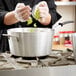 A chef using a Vollrath Wear-Ever sauce pan with a black silicone handle to cook on a stove.