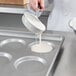 A person pouring white liquid into a Chicago Metallic hamburger bun pan.