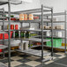 A metal shelving unit with five vented shelves, stocked with various food containers and kitchen supplies.