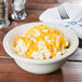 A Hall China ivory pot pie baking bowl filled with macaroni and cheese on a table with a fork and knife.