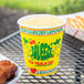 A yellow Squat "We Squeeze to Please" paper cup filled with lemonade on a table with fried chicken.