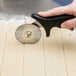 A person using an Ateco fluted stainless steel pastry cutter with a black handle to cut dough.