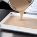 A person pouring brown liquid into a white tray using a MFG Tray half-size sheet pan extender.