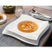 A Villeroy & Boch white porcelain pasta plate with a bowl of soup on a table.