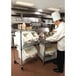 A chef in a commercial kitchen using a Rubbermaid white ingredient bin with sliding lid and scoop.