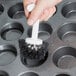 A person using an Ateco muffin pan cleaning brush to clean a muffin tin.