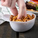 A person's finger grabbing a white mini baseball helmet bowl filled with pretzels.