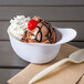 A white mini baseball helmet filled with ice cream with a cherry on top.