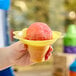 A hand holding a yellow plastic flower-shaped cup with a red and pink snowball in it.