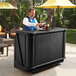 A man standing behind a Cambro portable bar with a drink.