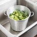 A Town aluminum colander filled with broccoli in a sink.