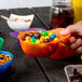 A person holding a bowl of assorted color mini baseball helmet ice cream bowls filled with candy.