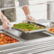 A person in a white uniform using a Vollrath stainless steel steam table pan to hold asparagus.