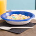 A Creative Converting cobalt blue paper bowl filled with cereal and a spoon.