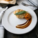 A Libbey alpine white porcelain plate with a piece of chicken, sauce, and a leaf on it.