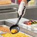 A person in gloves holding a black Vollrath Spoodle over macaroni and cheese in a white container.