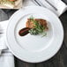 A Libbey alpine white porcelain plate with a piece of meat and a sprig of rosemary.