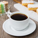 A cup of coffee on a Libbey alpine white porcelain saucer with pastries.