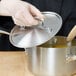 A person holding a Vollrath Miramar lid over a silver pot.