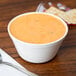 A white Carlisle polycarbonate bouillon cup filled with soup on a table.