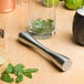 A Franmara stainless steel muddler with a tenderizer head muddling lime and mint leaves in a glass.