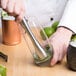 A hand using a Franmara stainless steel muddler to make a drink in a glass.