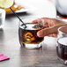 A hand holding a Chef & Sommelier Cabernet Rocks glass filled with liquid and ice, with a straw.