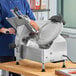 A woman in a blue uniform using a Centerline by Hobart automatic meat slicer to cut meat.