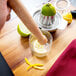 A hand using a Tablecraft Natural Wood Muddler to juice a lemon into a glass.