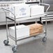 A Regency stainless steel utility cart with white boxes on it.