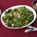 An American Metalcraft stainless steel oval bowl filled with salad, bread, and utensils.