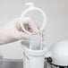 A gloved hand using the white plastic KitchenAid pasta press container.