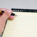 A hand writing with a pen on a yellow lined Docket writing pad.