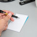 A hand holding a pen and writing on a white wirebound spiral notepad.