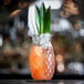 A Libbey pineapple cocktail glass filled with a drink and garnished with a green leaf.