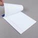 A person's hand holding a piece of college ruled paper from an Ampad writing pad.