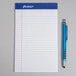 An Ampad College Ruled white notepad with a pen on top.