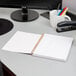 A black spiral bound planner on a desk with a pen in it.