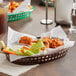 A brown Tablecraft oval platter basket of food on a table with a napkin.