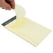 A hand holding a TOPS Docket narrow ruled yellow pad of paper.