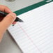 A hand holding a pen over a TOPS notebook filled with lined paper.